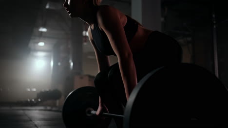 Slow-motion:-A-woman-lifts-a-barbell-in-a-dark-gym-with-a-lot-of-weight.-A-strong-young-woman-lifts-weights-for-a-workout